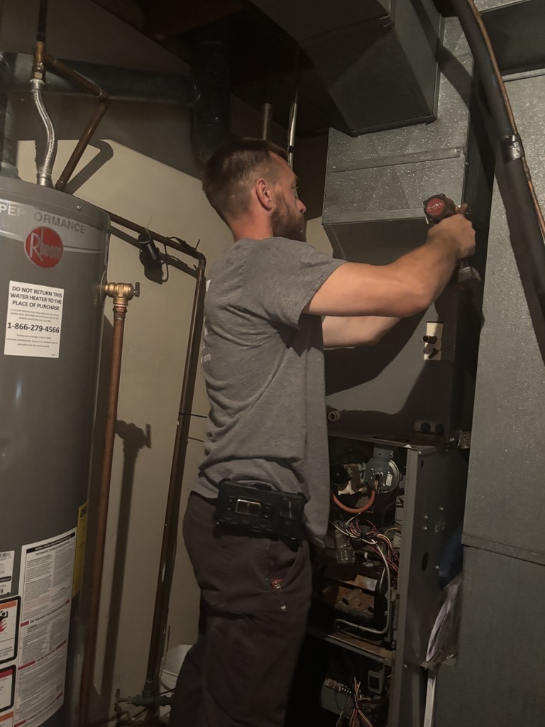 Walt Wright working on a furnace beside a water heater